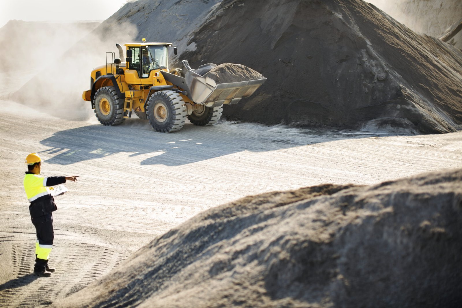 A man in a yellow vest stands beside a large dump truck, ready for work on a construction site.